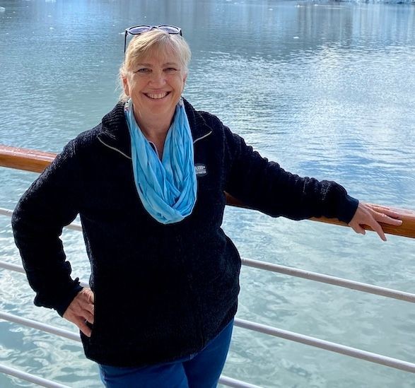 Kimberly Byerly, Luxury Travel Specialist, standing on the deck of a cruise ship in Alaska, smiling against a stunning backdrop of glacial waters.