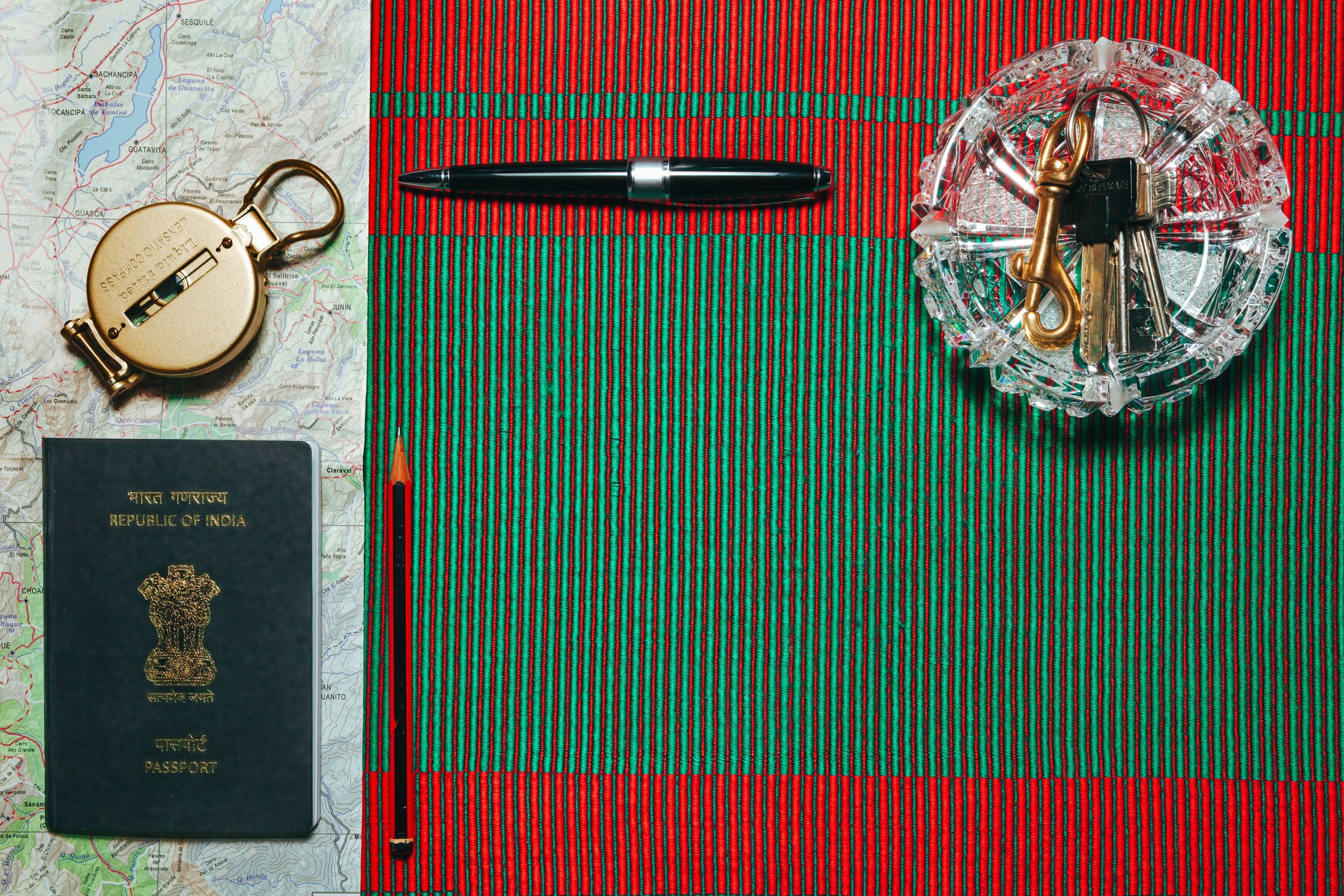 Passport, Map, Lensatic Compass, Pencil, Pen and Keys - Ready For A Long Drive In A Foreign Country. Flat Lay With Copy Space Displayed On A Woven Frbric Of Red And Green, Hinting At Christmas.