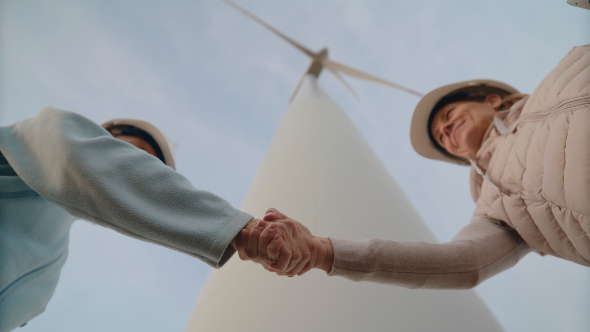 Female Engineers Exchanging Handshakes by Wind Turbines on Farm